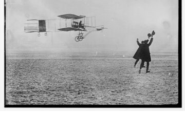 two men wave hats to greet pilot of flying past